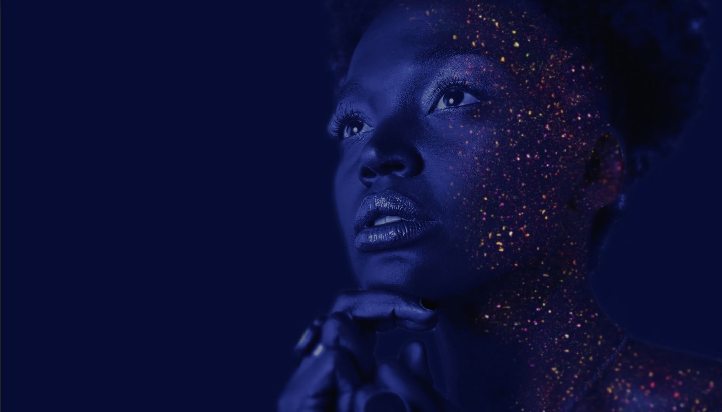 A woman with colorful lights on her face, looking up with a hopeful expression.